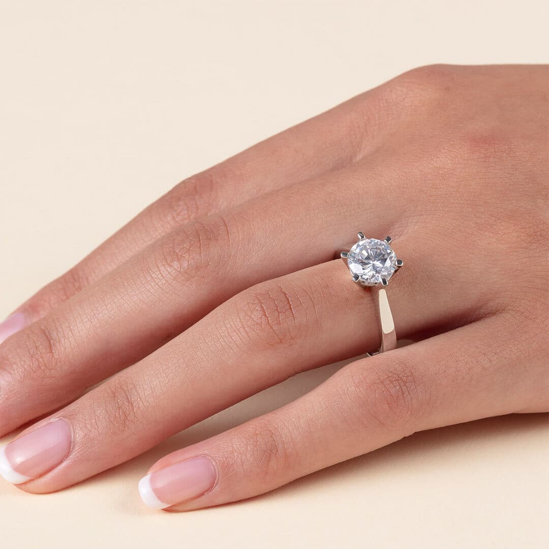 En hånd med pent manikyrerte negler som bærer en sølvring utsmykket med en stor, rund diamant på ringfingeren.