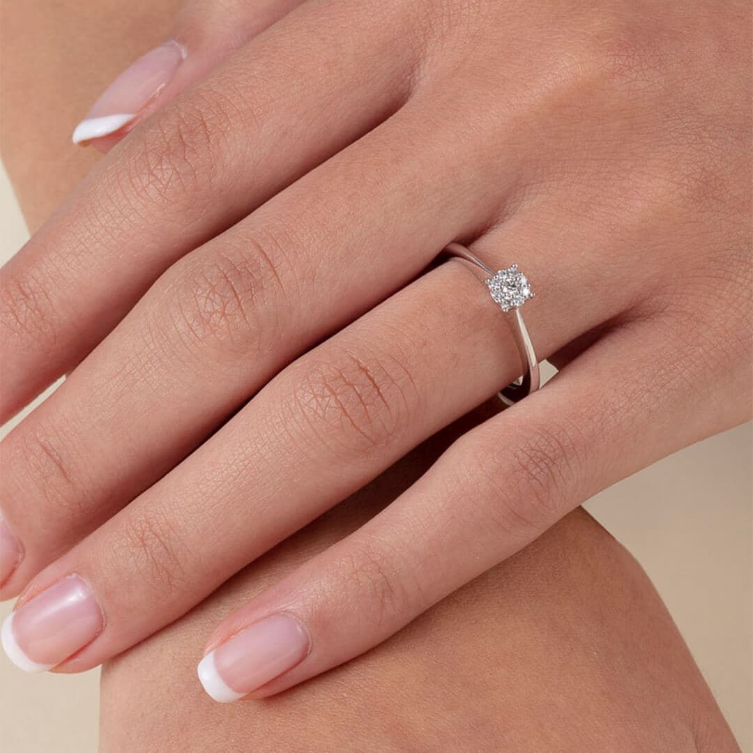 Nærbilde av en hånd med en solitær diamantring på ringfingeren, med velstelte negler med fransk manikyr.