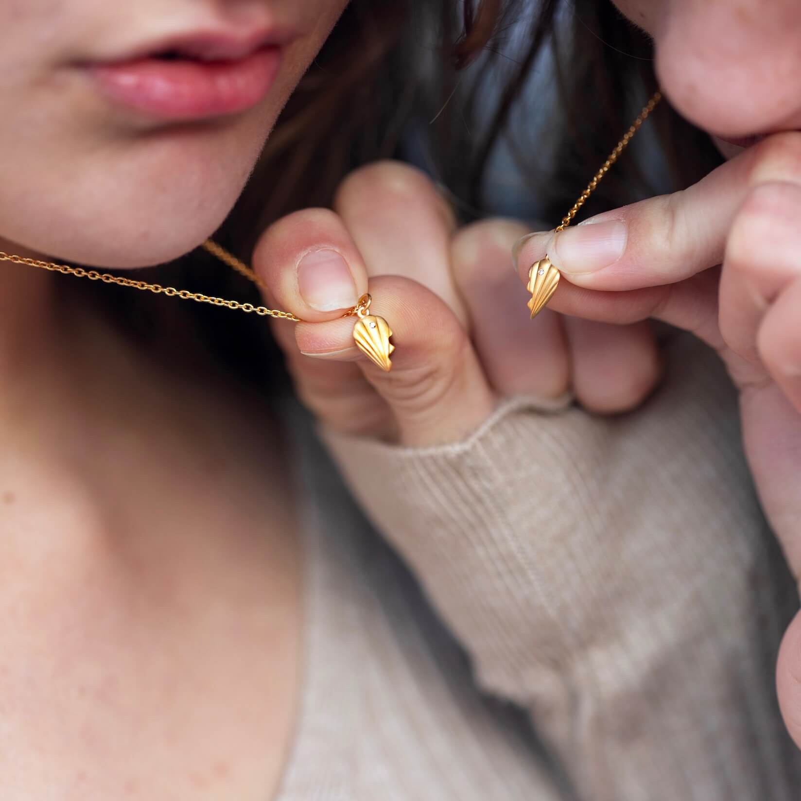To personer som holder matchende hjerteanheng i gull opp mot leppene, med fokus på detaljene i smykkene og deler av ansiktene deres.
