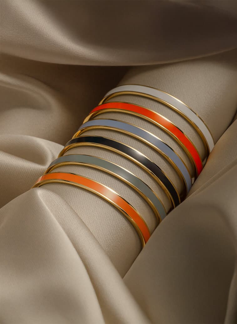 En stabel med fargerike armringer med gullkanter hviler på et glatt, beige stoff, noe som skaper en elegant og luksuriøs presentasjon.